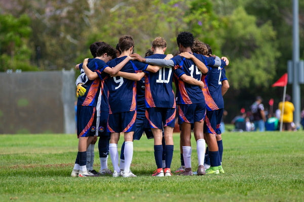 A soccer team huddles together on a green field.